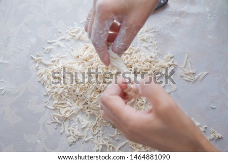 Young house wife preparing the homemade pasta at kitchen. Cutting long dough stripe for cooking pasta. Homemade food preparation concept. Closeup of process of making cooking homemade pasta. Erishte