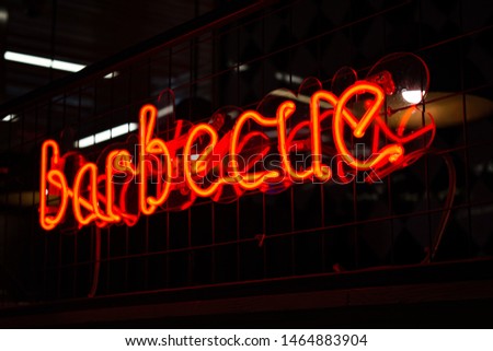 Glowing Neon red sign BARBECUE and blurred lights on black background. Dark tones vintage image.