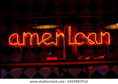 Glowing Neon red sign AMERICAN and blurred lights on black background. Dark tones vintage image.