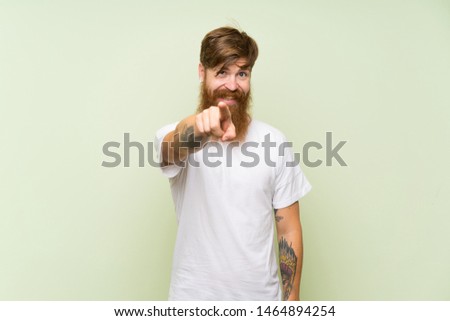 Redhead man with long beard over isolated green background points finger at you with a confident expression