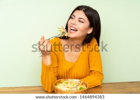 Happy Teenager girl with salad over green wall