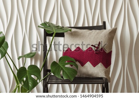 Designer pillow with knitted burgundy decor and sewn from natural linen fabric. Pillow rests on a black chair