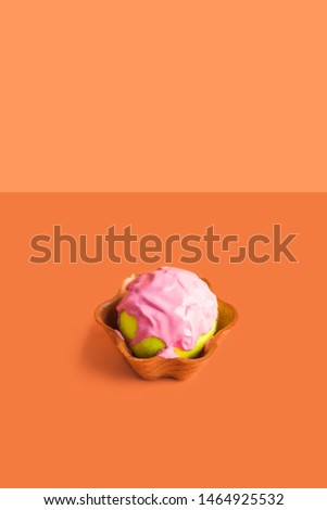 Tennis ball with pink paint as ice cream scoop in waffle cup on orange. Abstract art concept