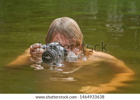 Voyeurist is taking pictures with waterproof camera during swimming in the river while having holiday.