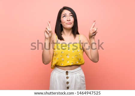 Young Mexican woman over isolated wall with fingers crossing and wishing the best