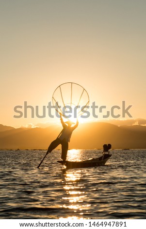 Vertical picture of burmese fisherman silhouette holding a traditional net at Inle Lake during sunset time, Myanmar