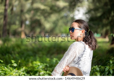 Young woman wearing a blue sunglasses with green tree background.