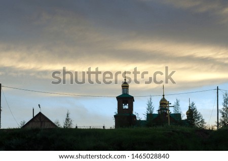 A wooden Church with Golden domes stands at sunset under the fat sky on a hill in the Northern village of Yakutia Suntar.