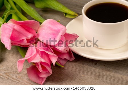 morning coffee in white porcelain cup and spring pink tulips bouquet over rustic wooden table
