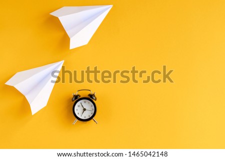 White paper planes and alarm clock on yellow background composition. Flat lay and top view photo