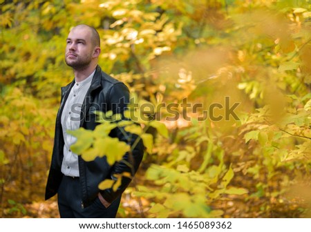 Man in the autumn forest. Bald brutal man standing in the autumn yellow forest looking away