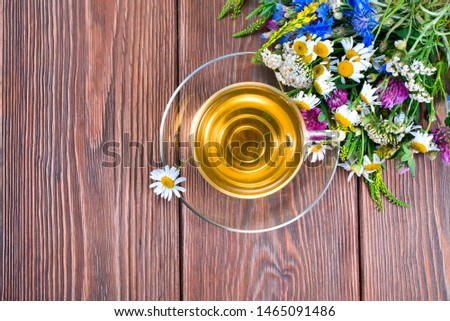 Herbal tea in a glass cup with bouquet of wild flowers on a wooden background. Text space. Top view.