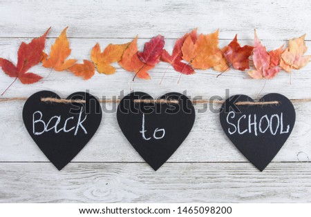 Back to school text on heart shaped blackboard pieces and fall leaves. White wooden background, garland, party. Education, September, autumn school concept