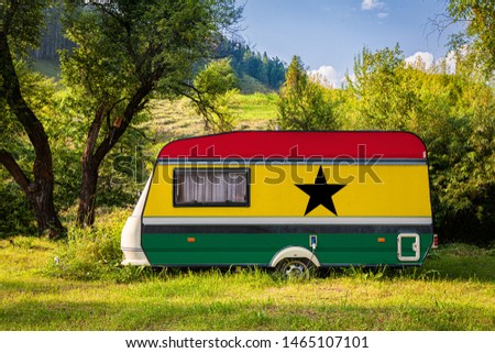 A car trailer, a motor home, painted in the national flag of Ghana stands parked in a mountainous. The concept of road transport, trade, export and import between countries. Travel by car