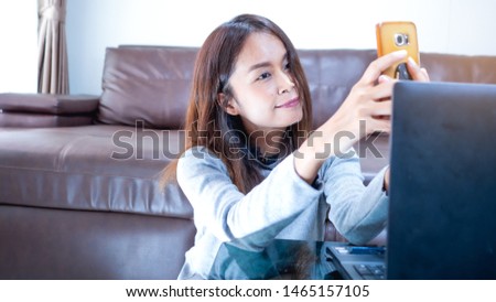 Beautiful Asian women sitting in the living room. She holds  mobile phone, Read phone messages, chat, Take a picture of yourself , Concept Technology and daily life.