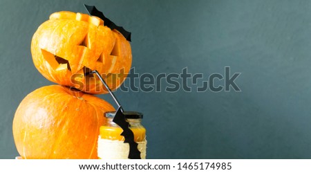 A glass of fresh pumpkin juice, decorated for Halloween with a flying bat, served with a straw pumpkin jack in the background. Dark background. Copy space.