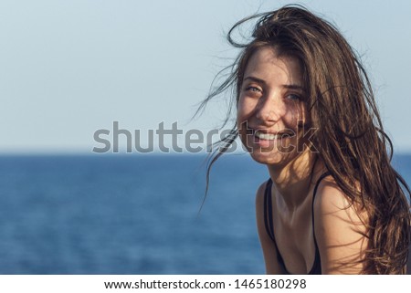 Close-up portrait of cheerful suntanned young woman over sea and blue sky background. Photo of beautiful brunette girl relaxing on the resort under the hot sun. Image of summer and vacation concept.