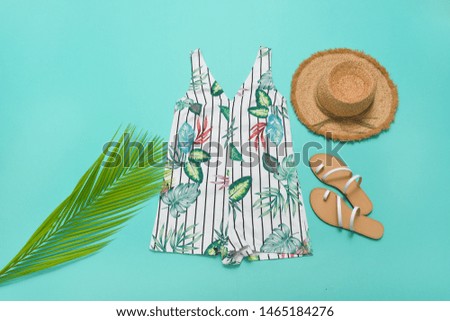 floral print with fern pattern.clothes and straw hat, green palm,shoes on blue background 

