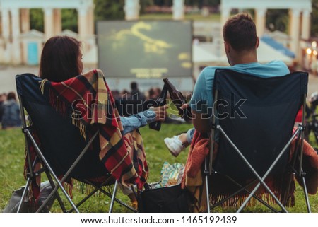 couple sitting in camp-chairs in city park looking movie outdoors at open air cinema lifestyle