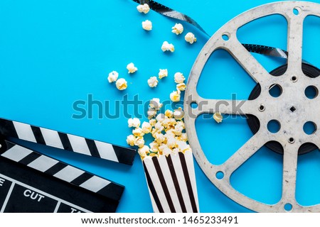 Filmmaker profession with clapperboard, popcorn and video tape on blue background top view copyspace
