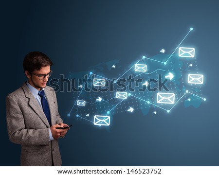 Attractive young man standing and holding a phone with arrows and message icons
