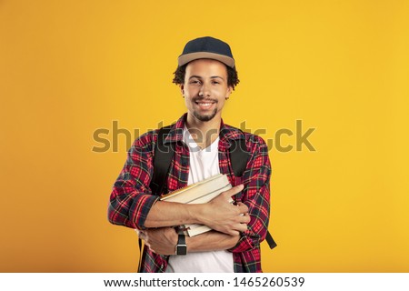 Picture of adult latino student over yellow background. Hold book in hands and smile. Standing alone. University time