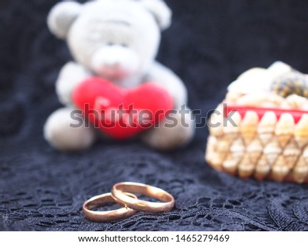 Little Bear with a red heart, two wedding rings and a box of shells on the background of black lace