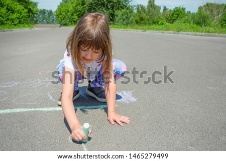 A little girl draws with chalk on an asphalt road. Concept - children's drawings of a picture on asphalt.