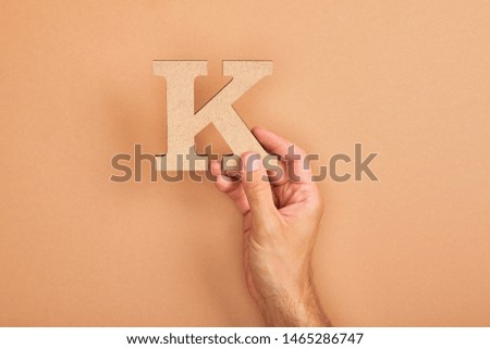 cropped view of man holding paper cut letter K on beige background