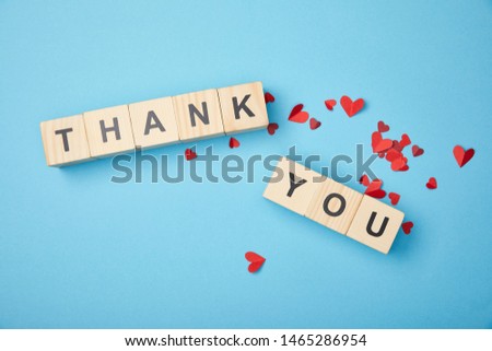 top view of wooden cubes with thank you words and red paper hearts on blue background