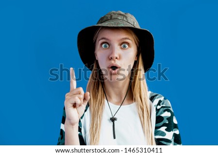 Ooh! Wow! Look at this! Pretty funny blonde woman showing one finger up with surprised shocked face. Copy spase over blue studio background. Funny ond joyfully picture. Fricky people 