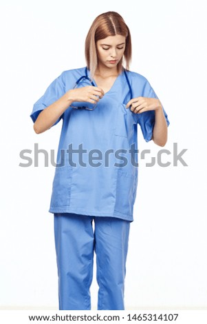 Woman doctor in a blue medical suit on a light background straightens a stethoscope around his neck