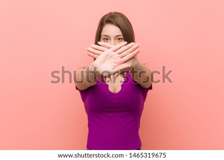 Young hispanic woman against a pink wall doing a denial gesture