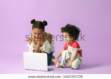 Cute African-American sisters with laptop watching cartoons on color background