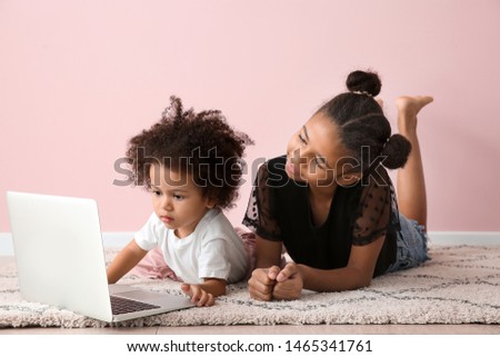 Cute African-American sisters with laptop watching cartoons near color wall