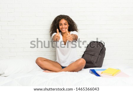 Young african american student woman on the bed with thumbs ups, cheers about something, support and respect concept.