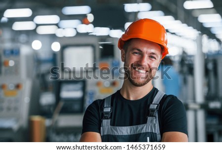 Smiling and happy employee. Portrait of industrial worker indoors in factory. Young technician with orange hard hat. Royalty-Free Stock Photo #1465371659