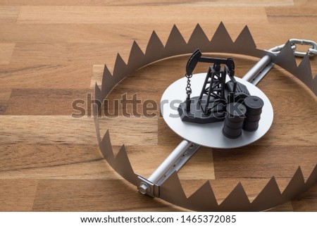 Oil pump jack and barrels in trap on wooden table background. Concept of crude oil petroleum trap in commodity market trading, bear market, investing risk management.