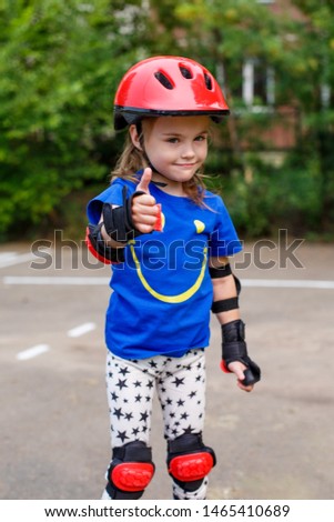 A small child in bright clothes, in a red helmet and protection on rollers on the road. Children's sport and active summer leisure.