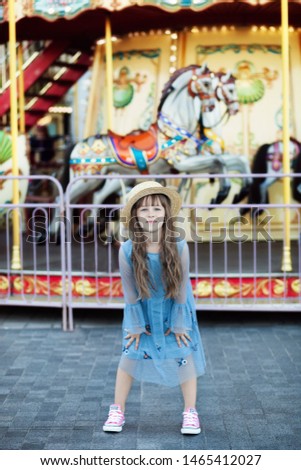Adorable little girl near the carousel outdoors. The girl on the carousel. Happy child having fun in the amusement park. Family weekend or vacation. Leisure with kids concept. happy childhood concept