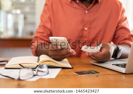 Closeup of african man hands using phone to calculate expenses. Man checking invoice balance on mobile phone app. Close up hands of black guy looking his budget and calculating credit card bills. Royalty-Free Stock Photo #1465423427