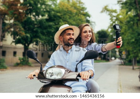 young couple driving scooter outdoor in city. taking picture with camera