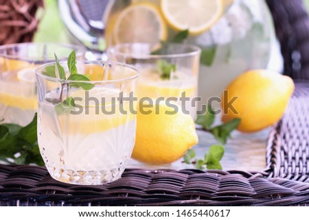 Glass of cool refreshing Southern Lemonade with mint and fresh lemons setting on a table outdoors.