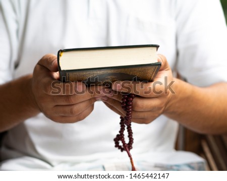 Young man holds Quran book. Islamic concept. Quran Kareem write with Arabic letters on the book cover