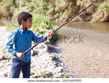 Portrait of little Afro-American boy fishing with rod on river