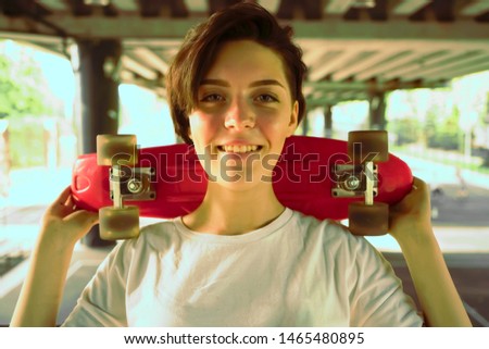 Portrait of a young happy beautiful woman with short hair. hipster girl in white t-shirt holding skateboard on shoulder. bridge background.Copy space.Lifestyle concept.