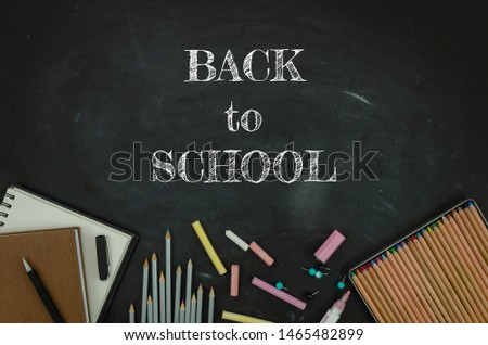 Flat lay tationery, notepads, pencils and clips over classroom blackboard with white chalk sign. Back to school concept
