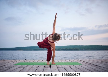 Beautiful young woman practices yoga on the wooden deck near the lake.
