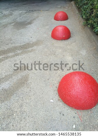 red hemisphere placed on the road to specify a border where you can not park. the road is filled with stains and some green bush is on the side