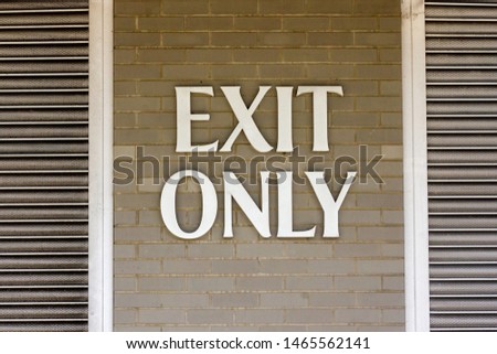 Exit only sign written in bold letters on a light brick wall